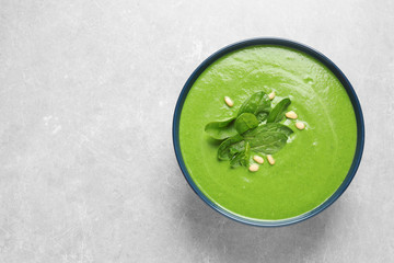 Bowl of healthy green soup with fresh spinach on grey table, top view. Space for text