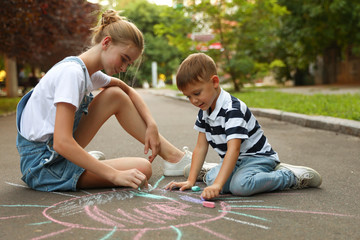 Teen nanny and cute little boy drawing sun with chalks on asphalt