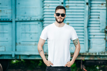 A young stylish man with a beard in a white T-shirt and glasses. Street photo