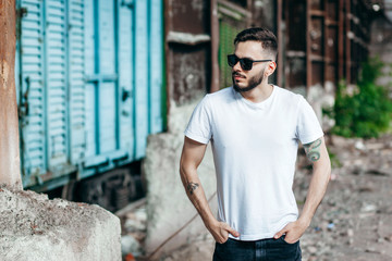 A young stylish man with a beard in a white T-shirt and glasses. Street photo