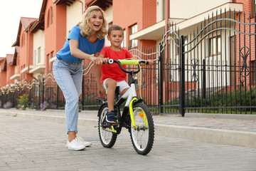 Obraz premium Happy mother teaching her son to ride bicycle in city