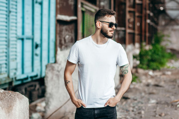 A young stylish man with a beard in a white T-shirt and glasses. Street photo