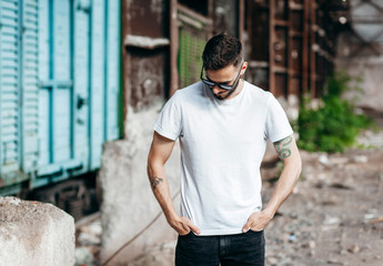 A young stylish man with a beard in a white T-shirt and glasses. Street photo