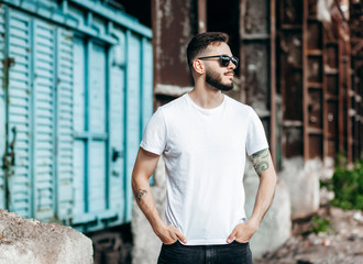A young stylish man with a beard in a white T-shirt and glasses. Street photo