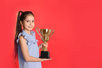 Happy girl with golden winning cup on red background. Space for text