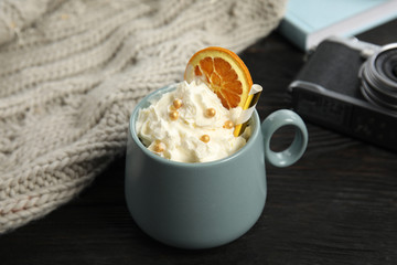 Cup of hot winter drink with whipped cream and knitted scarf on black wooden table