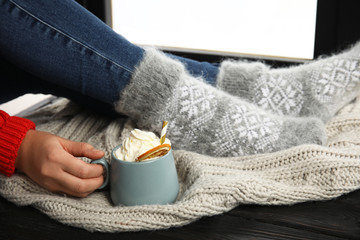 Woman with cup of hot winter drink with whipped cream sitting on window sill, closeup
