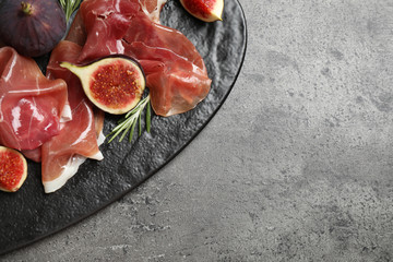 Delicious ripe figs and prosciutto served on grey table, top view. Space for text