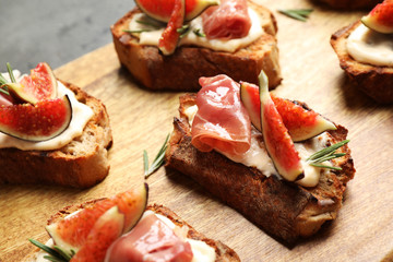 Bruschettas with cream cheese, prosciutto and figs served on wooden board, closeup