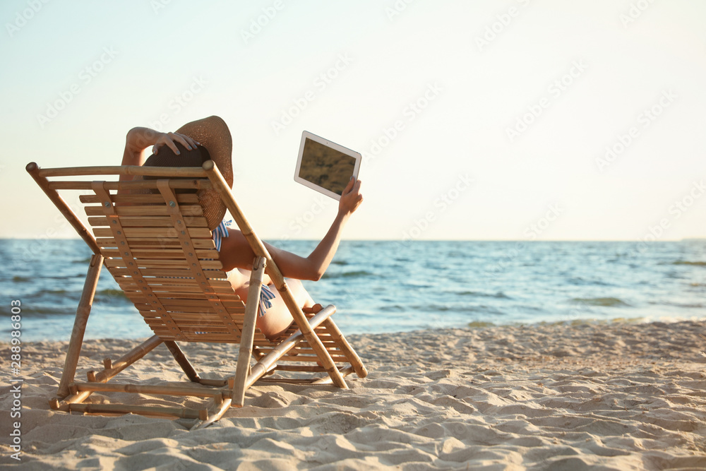 Sticker Young woman with tablet relaxing in deck chair on beach