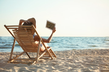 Young woman with tablet relaxing in deck chair on beach