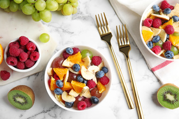Fresh tasty fruit salad on white marble table, flat lay