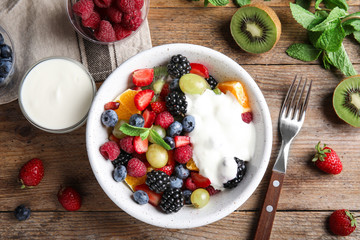 Fresh tasty fruit salad with yogurt on wooden table, flat lay