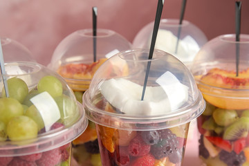 Fresh tasty fruit salad in plastic cups on pink background, closeup