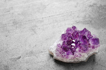 Beautiful purple amethyst gemstone on grey table, space for text