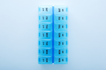 blue plastic 14 day pill box with pills on blue background. Top view.