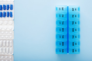 blue plastic 14 day pill box with pills on blue background. Top view.
