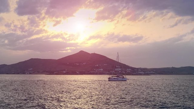 Amazing panorama of evening Paros island. Romantic sunset above Aegean sea, Cyclades islands. Yachts floating calm water. Sun going down behind the mountain. Peaceful tourist paradise, Greece