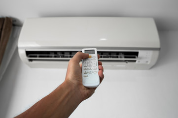 Man's hand using remote controler. Hand holding rc and adjusting temperature of air conditioner mounted on a white wall. Indooor comfort temperature. Health concepts and energy savings.