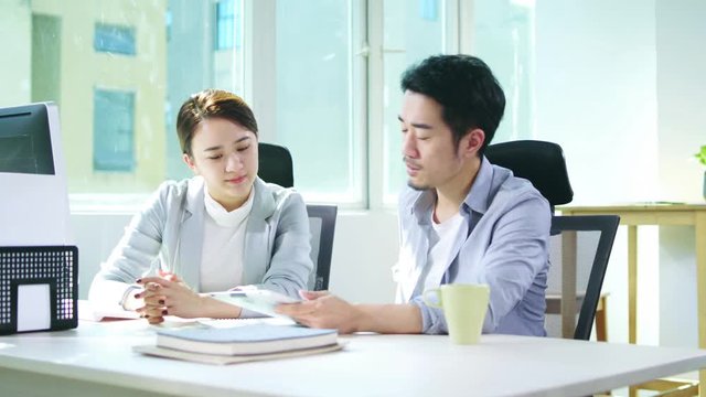 young asian man and woman sitting at desk working together discussing business plan