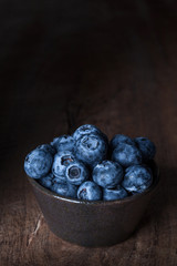 Blueberries in a brown ceramic bowl put on a wooden table with space for text.