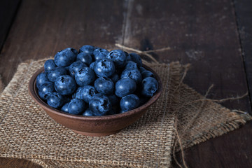 Blueberries in brown ceramic bowls placed on sacks and wooden tables with space for text.
