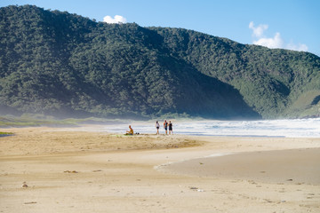 Fototapeta na wymiar personas caminando por la playa con unas montañas de fondo