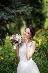 Emotional portrait of a happy bride in fashion wedding dress on natural background. Newlywed with a wedding bouquet in her hand laughs happily after the wedding ceremony. Wedding day.