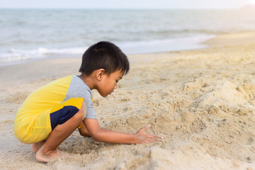 Portrait​ image​ of​ 5-6 years​ old​ Asian​ child​ boy​ playing​ the​ sand​ at​ the​ sea.​ Travel and​ development​ of​ kid​ concept.