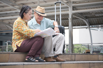 Asian Senior couple are sitting holding the map to search for destinations the streets of the big city. Elderly retired tourists spend the holidays to travel abroad. Travelers and lifestyle concept.