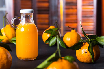 Suco Concentrado de tangerina na garrafa com as frutas sobre a mesa de madeira cor de carvão