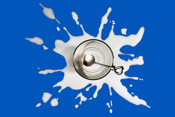 Vaso vacío sobre mancha de leche en fondo azul
