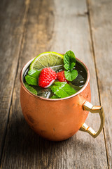 Raspberry and lime cocktail in copper mug (variation of Moscow mule) on the rustic background. Selective focus. Shallow depth of field.