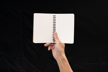 Man hand holding blank notebook on black background