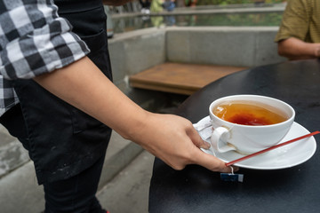 An asian or latina waitress tserving drinks of coffee and tea to customer in an outdoor cafe 