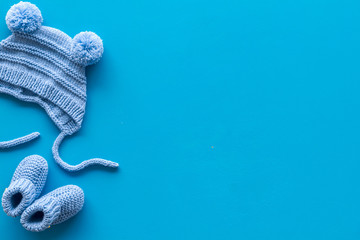 Booties and hat for newborn boy on blue background top view mockup