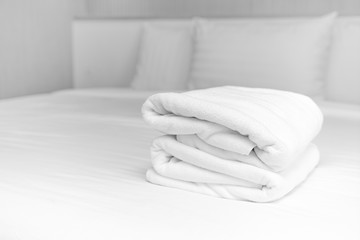 Close-up: The white towels are neatly folded and placed on the white bed. Hotel services
