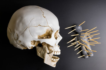 Voodoo doll with pins stuck into it and white skull on a black background with dramatic lighting.