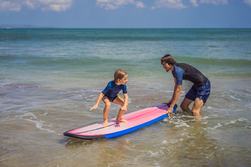 Father or instructor teaching his 5 year old son how to surf in the sea on vacation or holiday. Travel and sports with children concept. Surfing lesson for kids