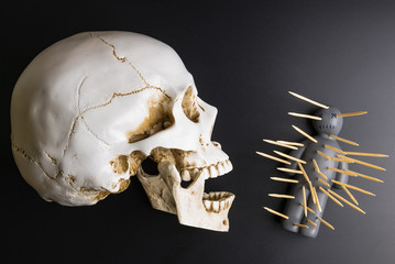 Voodoo doll with pins stuck into it and white skull on a black background with dramatic lighting.