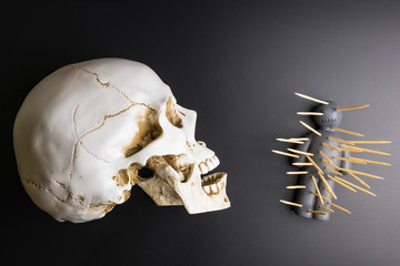 Voodoo doll with pins stuck into it and white skull on a black background with dramatic lighting.