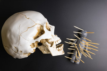 Voodoo doll with pins stuck into it and white skull on a black background with dramatic lighting.