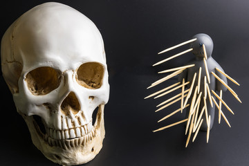 Voodoo doll with pins stuck into it and white skull on a black background with dramatic lighting.