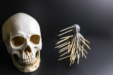 Voodoo doll with pins stuck into it and white skull on a black background with dramatic lighting.