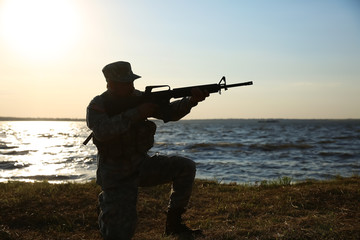 Silhouette of soldier in camouflage taking aim near river