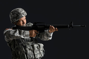 Mature male soldier aiming from assault rifle on dark background