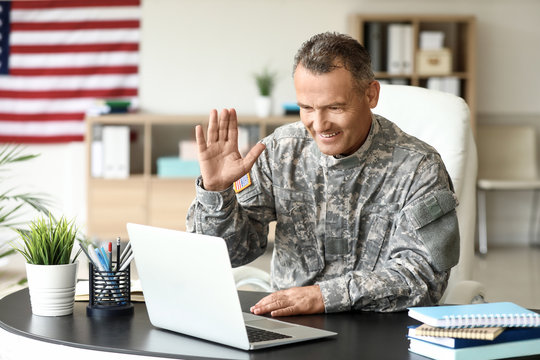 Mature male soldier using laptop in headquarters building for communication with his family