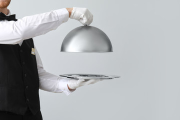 Handsome waiter with tray and cloche on light background - obrazy, fototapety, plakaty