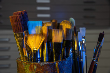 Container of artist brushes with creative lighting and file cabinet in background