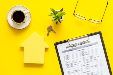 Fototapeta na wymiar Mortgage application with, glasses, coffee, house figure and keys on yellow background top view